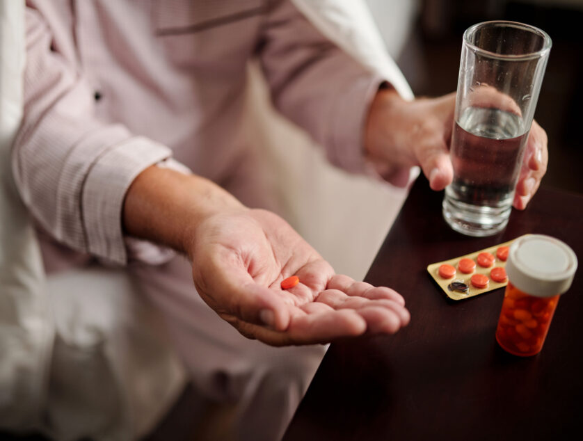 Sick Elderly Man Taking Pills Sick elderly man sitting in bed wrapped up in comforter and taking pills